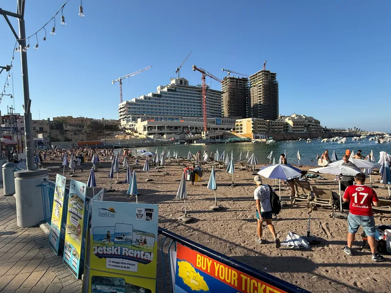 St George's Bay in July: sunbeds, jetski signs and towers going up behind. Fine for a quick dip, not worth crossing the island for